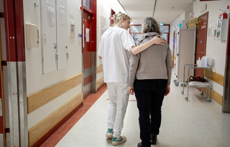 Bildet viser en sykepleier som støtter en pasient i en sykehusgang