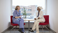 The photo shows two nurses sitting and talking together in front of a window