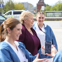 Bildet viser Ida Gerø med mobiltelefon, i bakgrunnen statsminister Erna Solberg og andre sykepleiere.